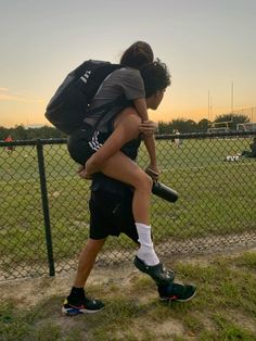 a woman carrying a man on her back while walking in front of a chain link fence