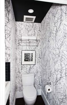 a white toilet sitting in a bathroom next to a wall papered with black and white trees