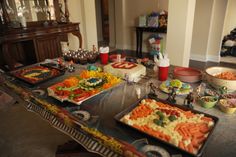 a table with many trays of food on it and plates in front of them