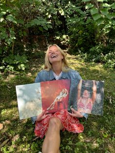 a woman sitting in the grass holding up some pictures with her mouth open and laughing