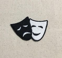 two theater masks embroidered on a white fabric background, one black and one white with the word theatre written across it