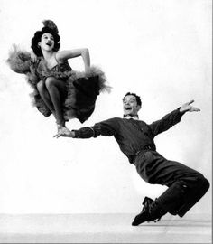 an old photo of two people jumping in the air with their legs spread out and one man is wearing a tuxedo