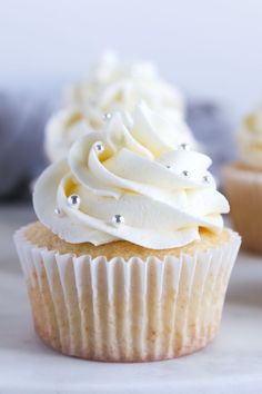 two cupcakes with white frosting and silver decorations