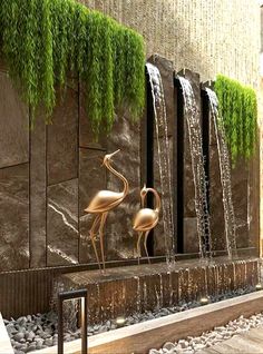 two flamingos are standing in front of a water fountain with green plants growing on it