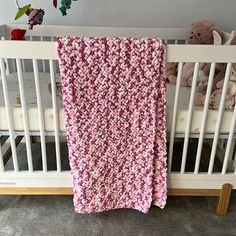 a crib with a pink and white blanket hanging from it's side next to a teddy bear