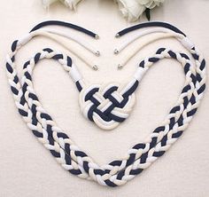 a white and blue heart shaped necklace with two braids on the bottom, surrounded by flowers