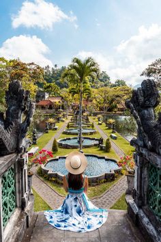 a woman in a hat is sitting on a bench looking at the water and garden