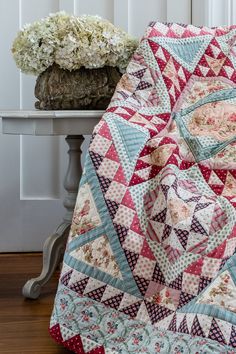 a pink and blue quilt sitting on top of a table next to a vase with flowers