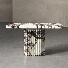 an artisticly designed marble table in the middle of a concrete floored room with grey walls