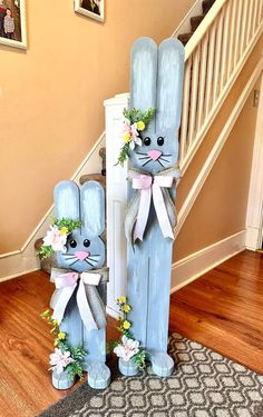 two wooden rabbits with flowers on their heads are standing in front of a stair case