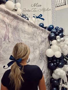 a woman standing in front of a wall with balloons and bows on it's head