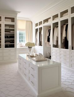 a walk in closet filled with lots of white cabinets and drawers next to a window