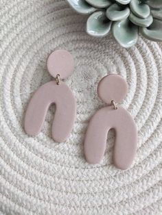 two pink earrings sitting on top of a white table next to a potted plant