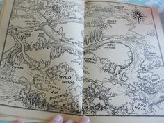 a hand holding an open book with a map in the middle and trees on it