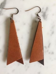 two pairs of brown leather earrings on a marble surface