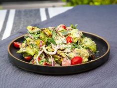 a black plate filled with salad on top of a blue table cloth next to a pool