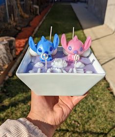 someone is holding up a small tray with two little figurines in it and some marshmallows on top