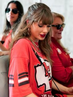 two women in red shirts are sitting on a couch and one is using a cell phone