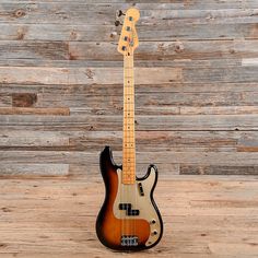 an electric bass guitar sitting on top of a wooden floor next to a wood wall