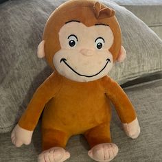 a stuffed monkey sitting on top of a couch next to a gray pillow with a smiling face