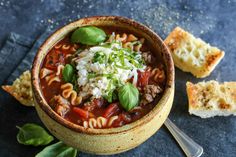 a bowl of pasta soup with spinach, cheese and bread slices on the side