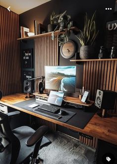 a desk with a monitor, keyboard and speakers on it in front of a wooden wall