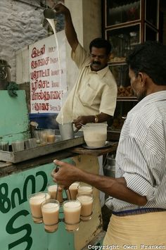 two men are making drinks in front of a food stand that sells milkshakes