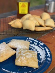 some pastries are on a blue plate with powdered sugar and honey in the background