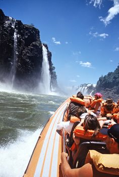 a group of people riding on the back of a boat in front of a waterfall