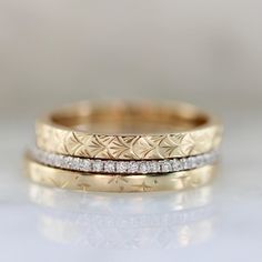 two gold wedding bands with diamonds on top of each other, sitting on a white surface