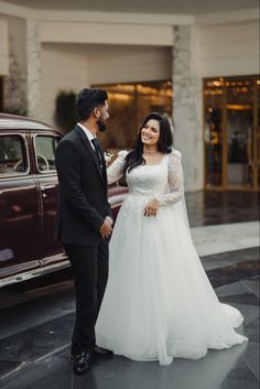 a bride and groom standing next to an old car in front of a hotel lobby