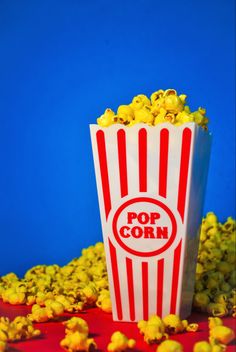 a red and white striped popcorn bag filled with yellow popcorn kernels on a blue background