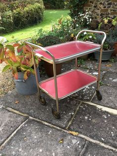 a red cart sitting on top of a sidewalk next to a potted plant