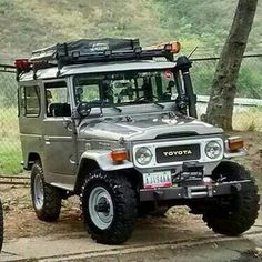 two jeeps parked next to each other on the side of a road with trees in the background