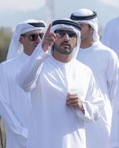 a man in white is pointing to the side with other men standing behind him and wearing sunglasses