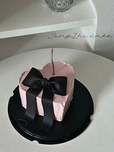 a pink and black heart shaped cake with a bow on the top sitting on a table