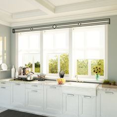 a kitchen with white cabinets and counter tops in front of two large windows that have sun shining through them