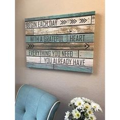 a blue chair sitting next to a vase with flowers in it and a wooden sign on the wall