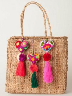 a straw bag with colorful tassels hanging from it's handles and two small pom poms attached to the handle