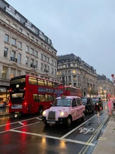 a red double decker bus driving down a street next to tall buildings on a rainy day