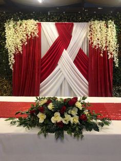 a white and red table cloth with flowers on it next to a wall covered in greenery