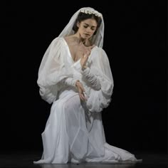 a woman in white dress sitting on the floor with her hands clasped to her chest