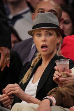 a woman in a hat is holding a drink and looking surprised at the basketball game