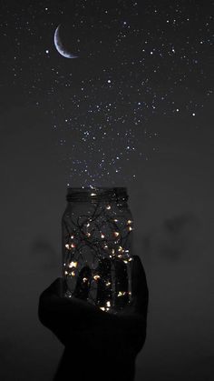 someone is holding up a jar with lights in it and the stars are falling from the sky