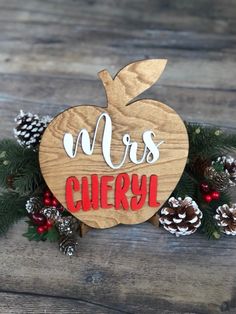 a wooden sign that says mrs cherry with pine cones and berries around it on a table