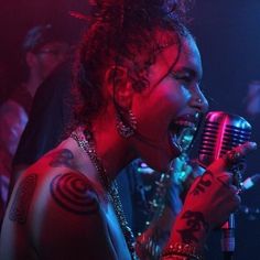 a woman singing into a microphone with tattoos on her arm