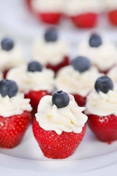 strawberries with white frosting and blueberries on top are arranged on a plate