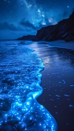 an ocean beach with blue lights on the water and stars in the sky above it