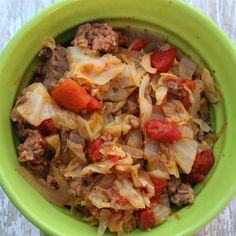 a green bowl filled with meat and vegetables on top of a wooden table next to a fork