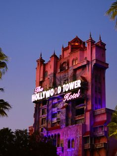 the hollywood tower hotel is lit up in purple and pink colors at night time with palm trees surrounding it